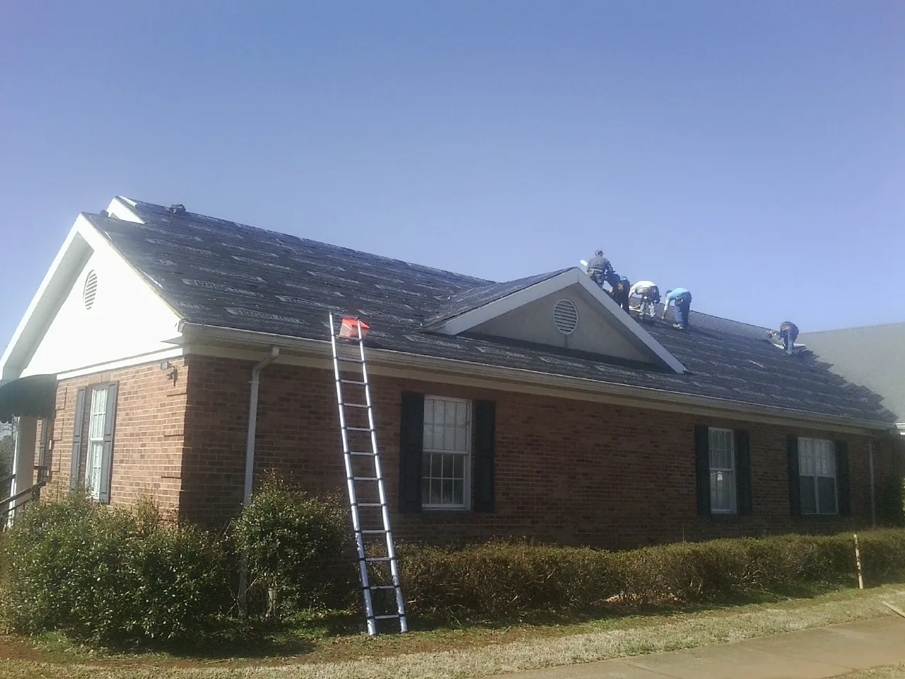 Crew tearing shingles off a brick ranch roof with a ladder set — Metal Roof Repair work by our crew in Fairmont